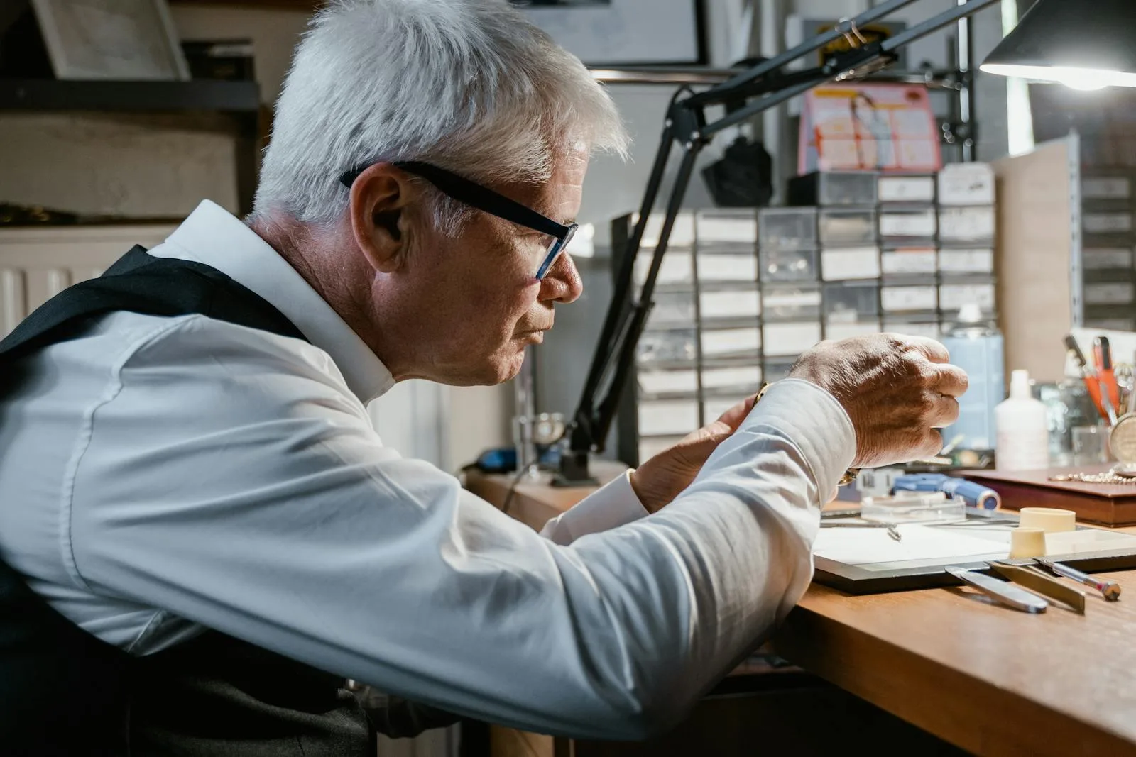 Elderly watchmaker concentrating on watch repair in a detailed workshop setting.