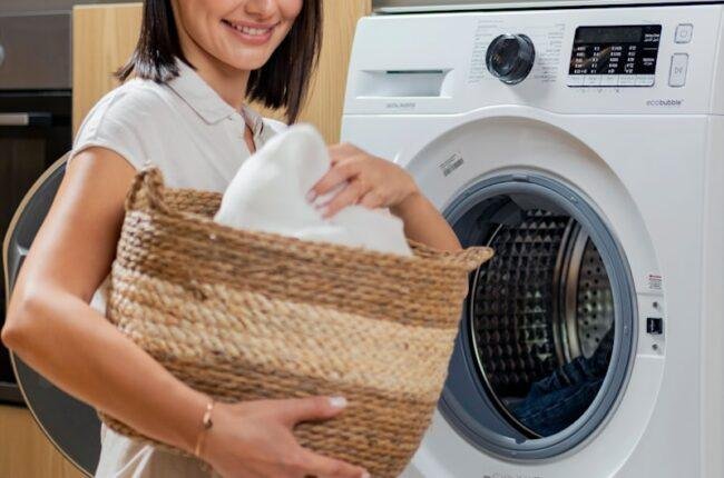 a woman is holding a basket near a washing machine